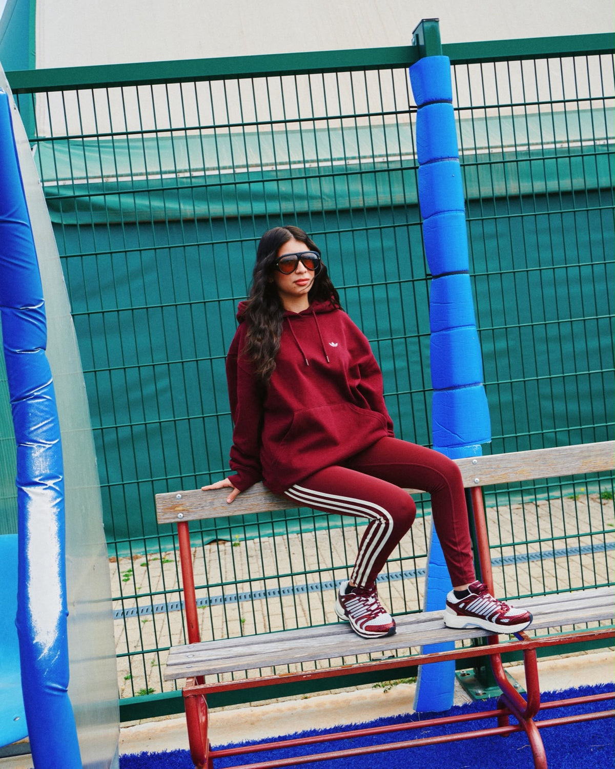 Ragazza con felpa e leggings Adidas bordeaux seduta su una panchina
