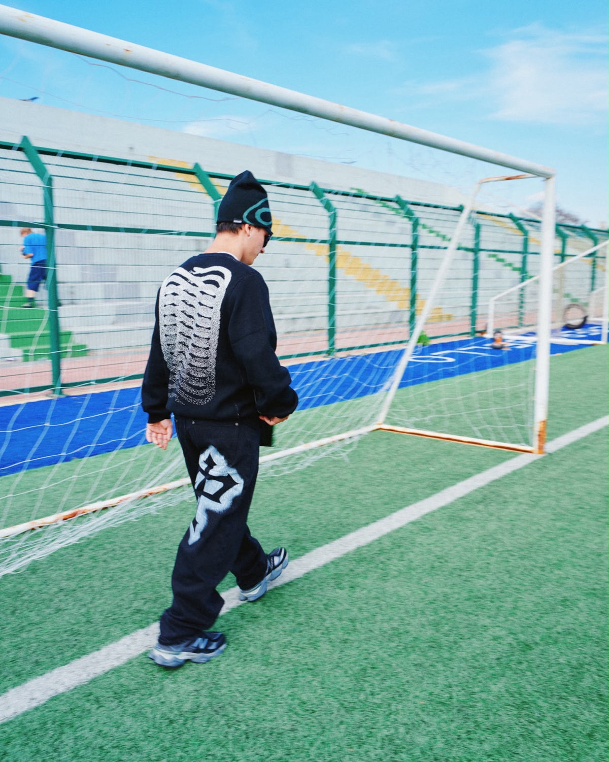 Ragazzo di spalle con felpa nera, beanie e New Balance davanti alla porta
