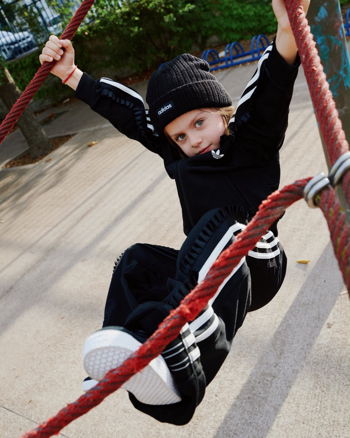 Bambino in tuta Adidas nera appeso alle corde di un parco giochi